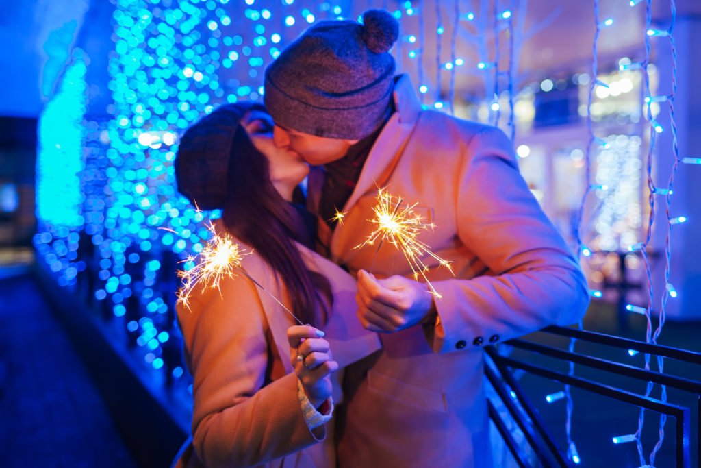 Young loving couple burning sparklers by holiday illumination. Christmas and New year concept